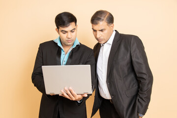 Two indian businessman wearing black formal suit working on laptop isolated over beige background. Business and corporate concept.