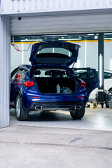 The rear view of a blue car with an open trunk and doors standing in a garage detailing car repair