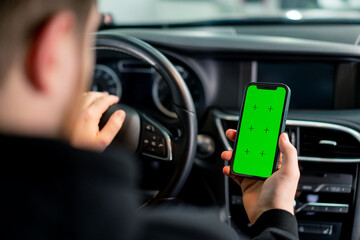 A man sits in a luxury car with a green screen phone in his hands