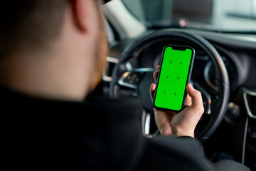 A man sits in a luxury car with a green screen phone in his hands