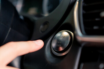 A man presses the start button of his luxury car black car interior