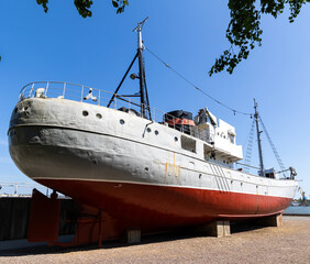 Naklejka premium A historic fishing boat pulled out of the water and displayed on the museum's quay. Shot taken on a sunny day, the ship against the blue sky...