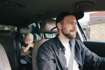 A man driving a car and a small child toddler in the back seat in a car seat
