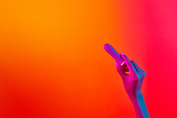 Woman's hand holding vibrator, massager over yellow-pink background in neon light. Concept of toys...