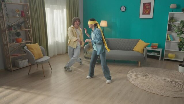 A young married couple spends time together, having fun. A couple is playing a game of blind man's buff. A blindfolded Asian woman catches a man dodging her. HDR BT2020 HLG Material.