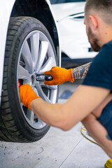 Auto mechanic man changing a wheel on a luxury white car using a balloon wrench at a car service station close-up © Guys Who Shoot