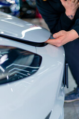 A man is in pain pinching his fingers under the hood of his white luxury car in a parking lot or car service close-up