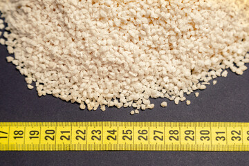 wheat, heap of wheat flakes next to measuring tape, black background, generated with extruder machine