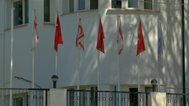 Few flags hanging in a row and are at the top of the pole in front of a building. three of them are Turkish flags and the building is at the border of the Turkish side of Nicosia, Cyprus capital city.