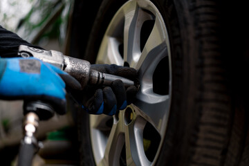 Fototapeta premium Auto mechanic changing a wheel from a black car using a drill in a tire shop on the street detailing car repairs