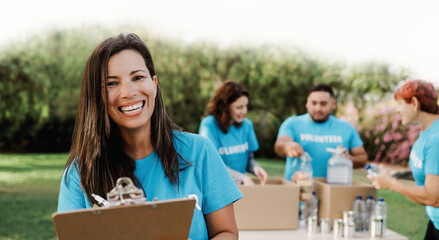 Latin female volunteer working with group of people for food collection community service outdoors - Donations and charity project concept