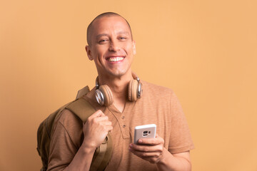 joyful college student smiling and holding mobile phone in beige studio background. back to school, student life concept.