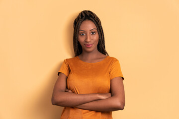 serious afro brazilian woman with arms crossed in beige background. portrait, real people concept.