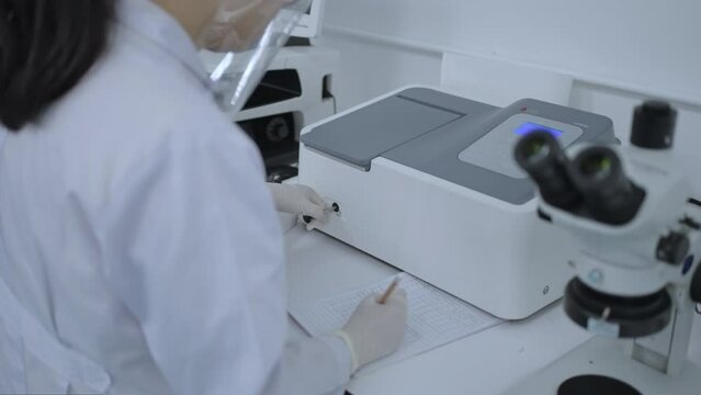 Chemical research scientists use uv visible spectroscopy to check the absorbance and keep the test results in a notebook, Analyze data and collect chemical test results in modern laboratories.