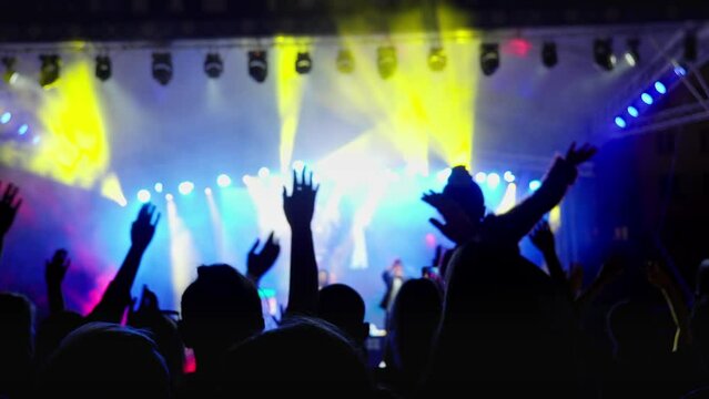 Silhouette hands of audience crowd people enjoying the concert. People with raised arms on music live event. People jumping and dancing at party concert with lightshow. 4K, UHD