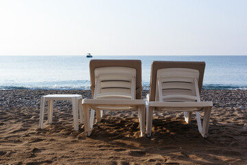 Two sun loungers and a table on a beach. Blue sea background. Silhouette of motorboat on the horizon. Vacatoin concept
