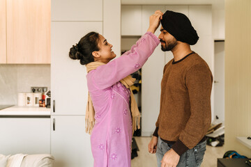 Young indian woman fixing turban on head of her husband