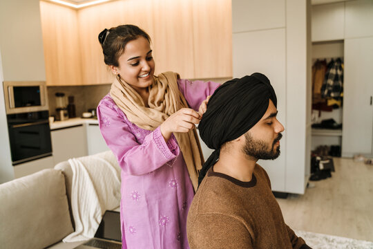 Young happy smiling indian woman putting turban on her husband