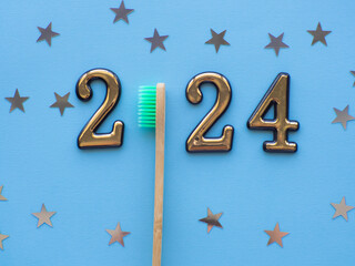 2024 and dental concept. Close up view photo with 2024 and wooden green toothbrush instead zero on blue background with copy space for text. Christmas medical card. Merry Christmas and Happy New Year