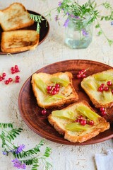 Dessert or breakfast, fried toast with rhubarb in sugar syrup and fresh red currants on a brown plate on a beige concrete background. Seasonal recipes, rhubarb dishes.