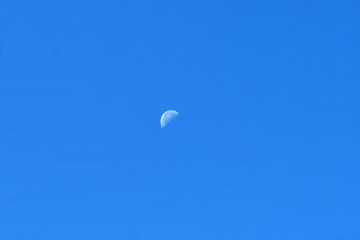 A pale spot of the moon against the blue sky.