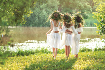 Three girls in white dresses with a wreath of flowers are celebrating Ivan's Day or Ivan Kupala's holiday.