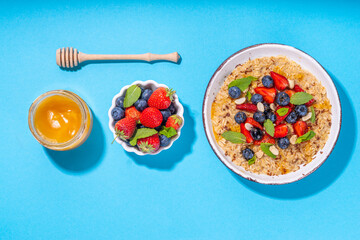 Summer breakfast oatmeal with strawberry, blueberry, nuts, chocolate and honey top view copy space, traditional summer fruit and berry oats porridge
