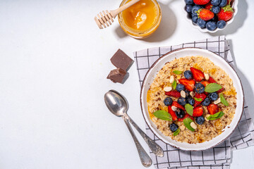 Summer breakfast oatmeal with strawberry, blueberry, nuts, chocolate and honey top view copy space, traditional summer fruit and berry oats porridge