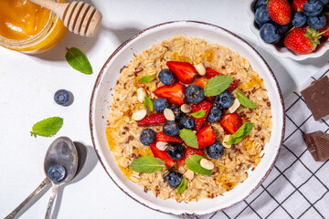 Summer breakfast oatmeal with strawberry, blueberry, nuts, chocolate and honey top view copy space, traditional summer fruit and berry oats porridge