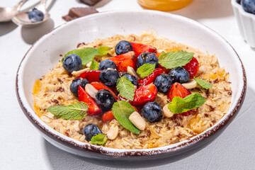 Summer breakfast oatmeal with strawberry, blueberry, nuts, chocolate and honey top view copy space, traditional summer fruit and berry oats porridge