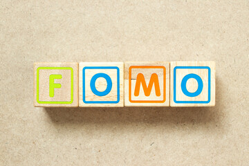 Wooden alphabet letter block in word FOMO (abbreviation of fear of missing out) on wood background