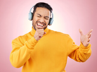 Asian man, headphones and listening to music while singing for karaoke against a pink studio background. Happy male person enjoying online audio streaming, sound track or songs with headset on mockup