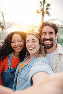 Vertical portrait. Group of young adult friends smiling taking a selfie portrait and having fun together. Group of people celebrating their friendship. Two women and one man with positive expression
