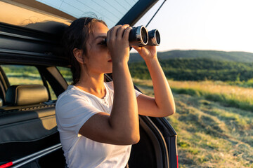 a young woman is sitting in the trunk of her car and using binoculars