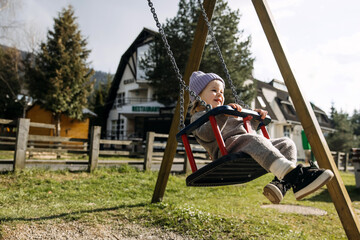 Child on swing at a playground on spring sunny day, smiling.