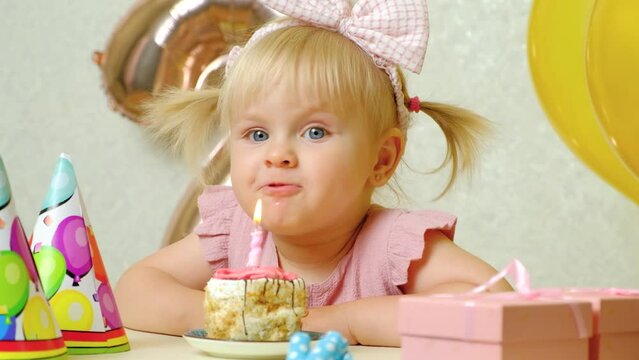 A two-year-old girl blows out a candle on a birthday cake, makes a wish