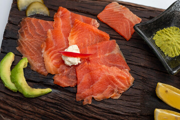 smoked salmon in fresh slices on a rustic wooden board with wasabi avocado, cheese, lemon pickles and soy sauce