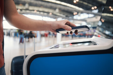 Hand of man during using self service check-in machine. Passenger scanning ticket on smart phone at...