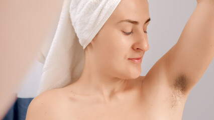 Happy smiling woman in bath towel looking on her hair growing under arms. Concept of beautiful female, natural beauty, feminity and body hair.
