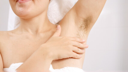 Closeup of long dark hair growing under arms of young woman standing at bathroom mirror. Concept of beautiful female, natural beauty, feminity and body hair.