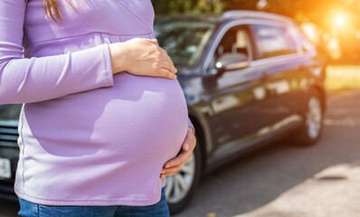 A pregnant girl with a big belly in a purple sweater on the background of a car. The concept of...