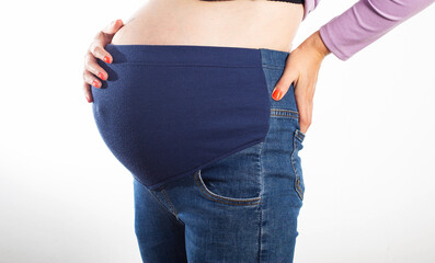 Pregnant girl with a big belly in jeans on a white background. The concept of comfortable clothes for pregnant women, universal elastic in jeans.