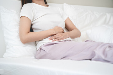 Close-up woman feeling stomach pain from cycle period on the bed at home.