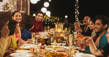 Big Indian Family Celebrating Diwali: Family Gathered Together on a Dinner Table in a Backyard Garden Full of Lights. Group of People Sharing Food, Laughs and Stories on a Hindu Holiday