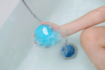 Fototapeta premium Bath bomb blue with coconut extract in the form of a heart in the hand of a child. Cosmetics and skin care. Copy space for text