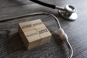 Stethoscope and wooden cubes with text AUTONOMY, BENEFICENCE, NON-MALEFICENCE, and JUSTICE. The...