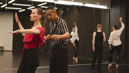 Medium slowmo of beautiful young Caucasian woman wearing red top and lips practicing Latin dance movements while having lesson with Biracial male teacher in spacious dance class - Powered by Adobe