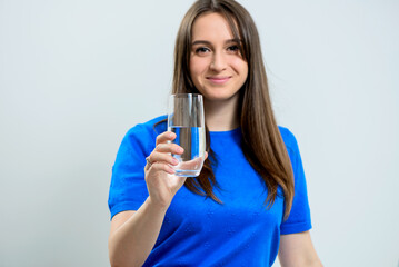 Young smiling woman in blue dress holding a glass of crystal clear water ready to drink