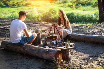 Young caucasian guy and girl sit on logs in nature and communicate. Outdoor recreation in summer, relaxation.