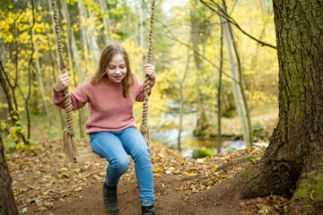 Pretty young girl having fun on a playground in beautiful autumn park. Cute preteen child playing outdoors in late autumn.